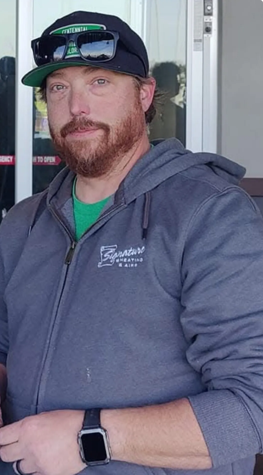 Man with beard wearing black cap, gray hoodie, and smartwatch
