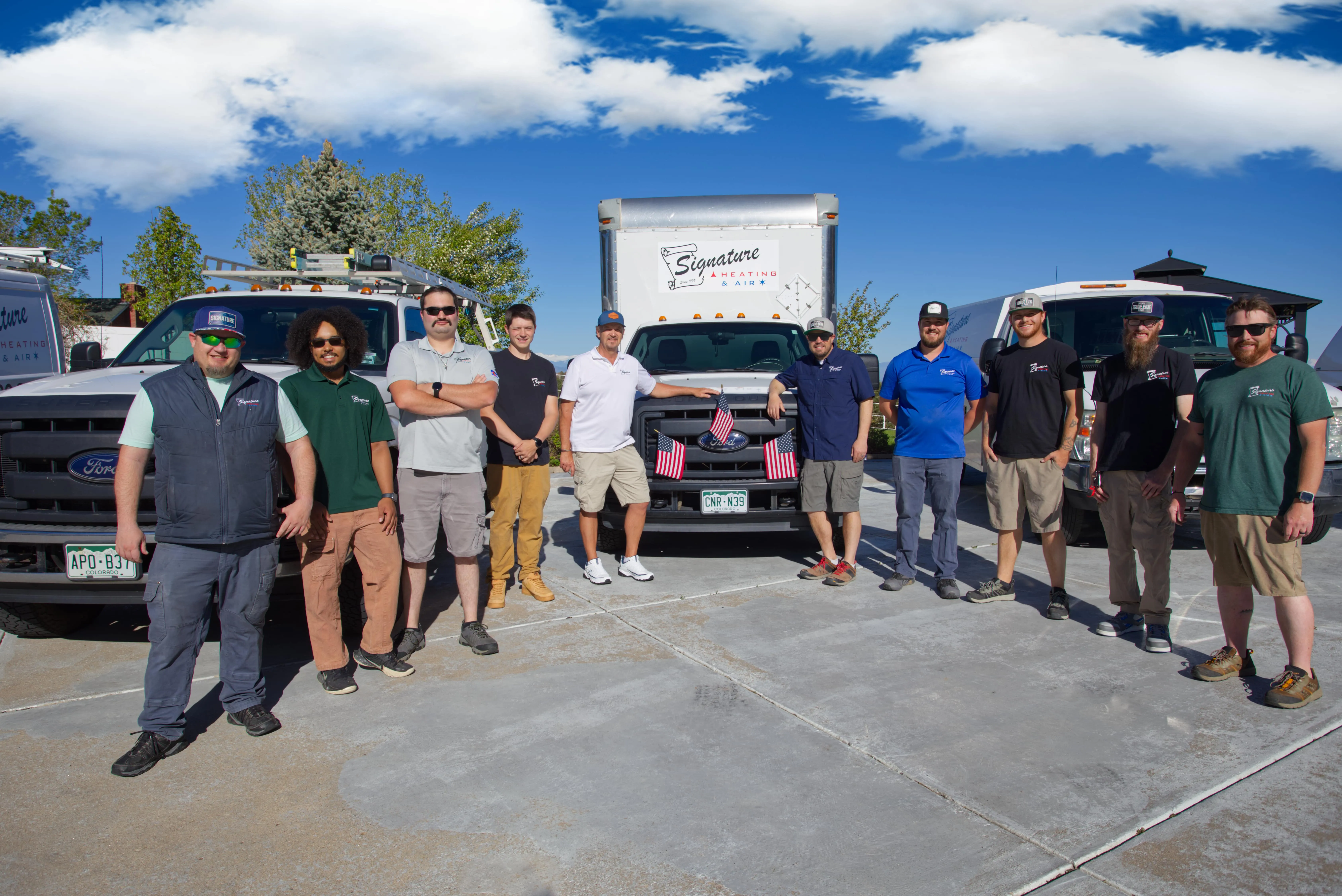Signature HVAC team posing with company trucks on sunny day