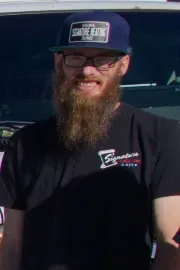 Bearded man in baseball cap and black shirt smiling outdoors