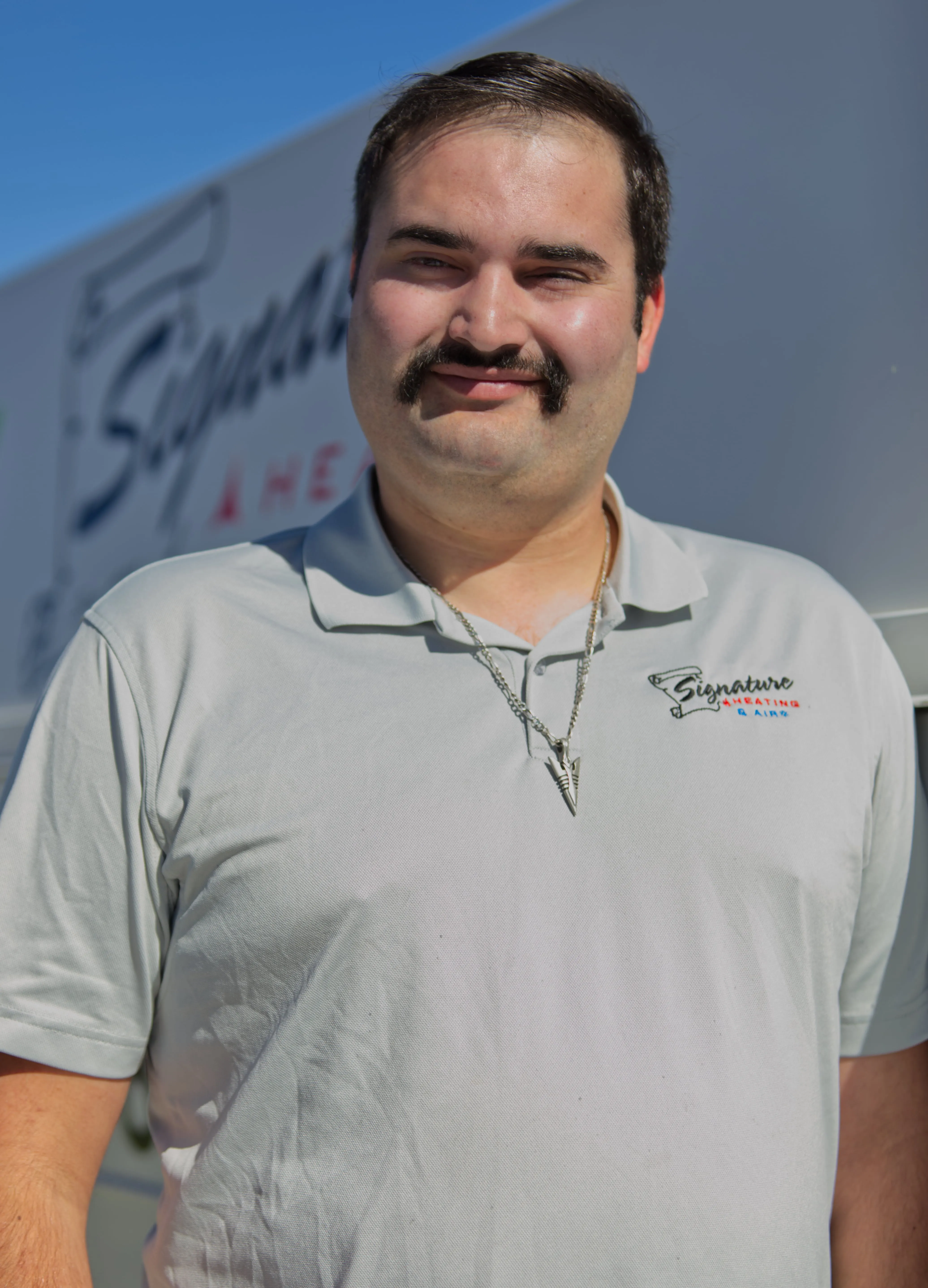 Employee in white polo shirt with Signature logo smiling outdoors