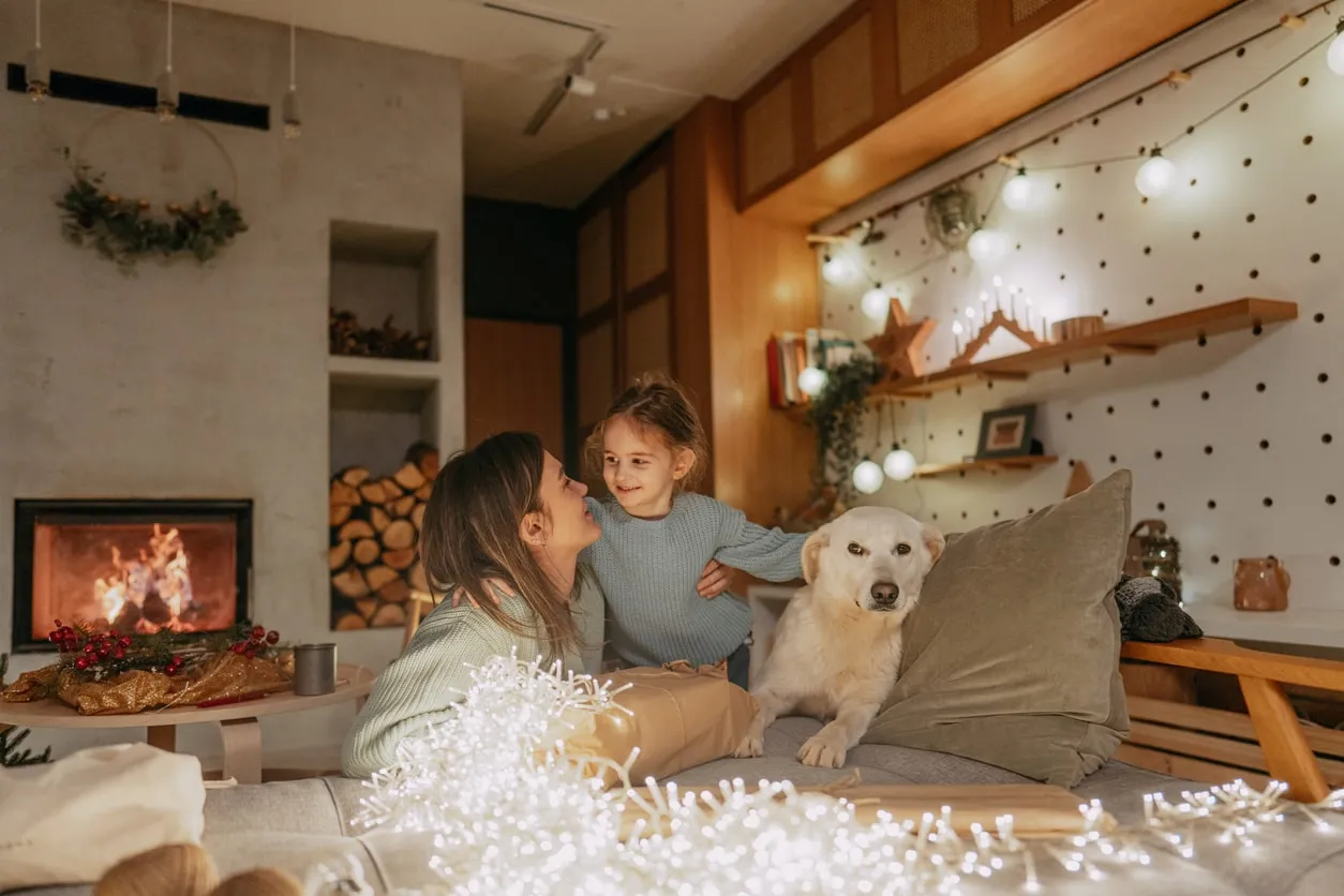 Mother and daughter with dog enjoy cozy Christmas time by fireplace