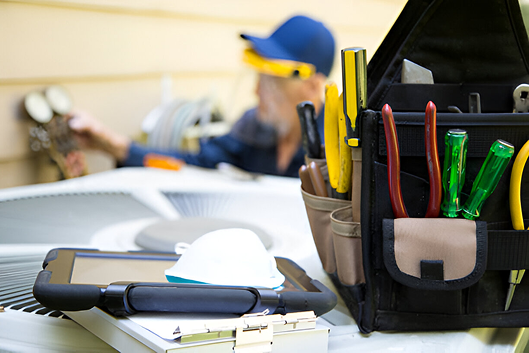Toolbag with colorful tools and clipboard on worksite with worker