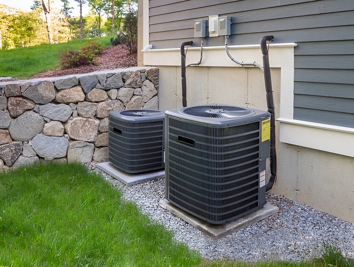 Two air conditioning units next to stone wall and green lawn