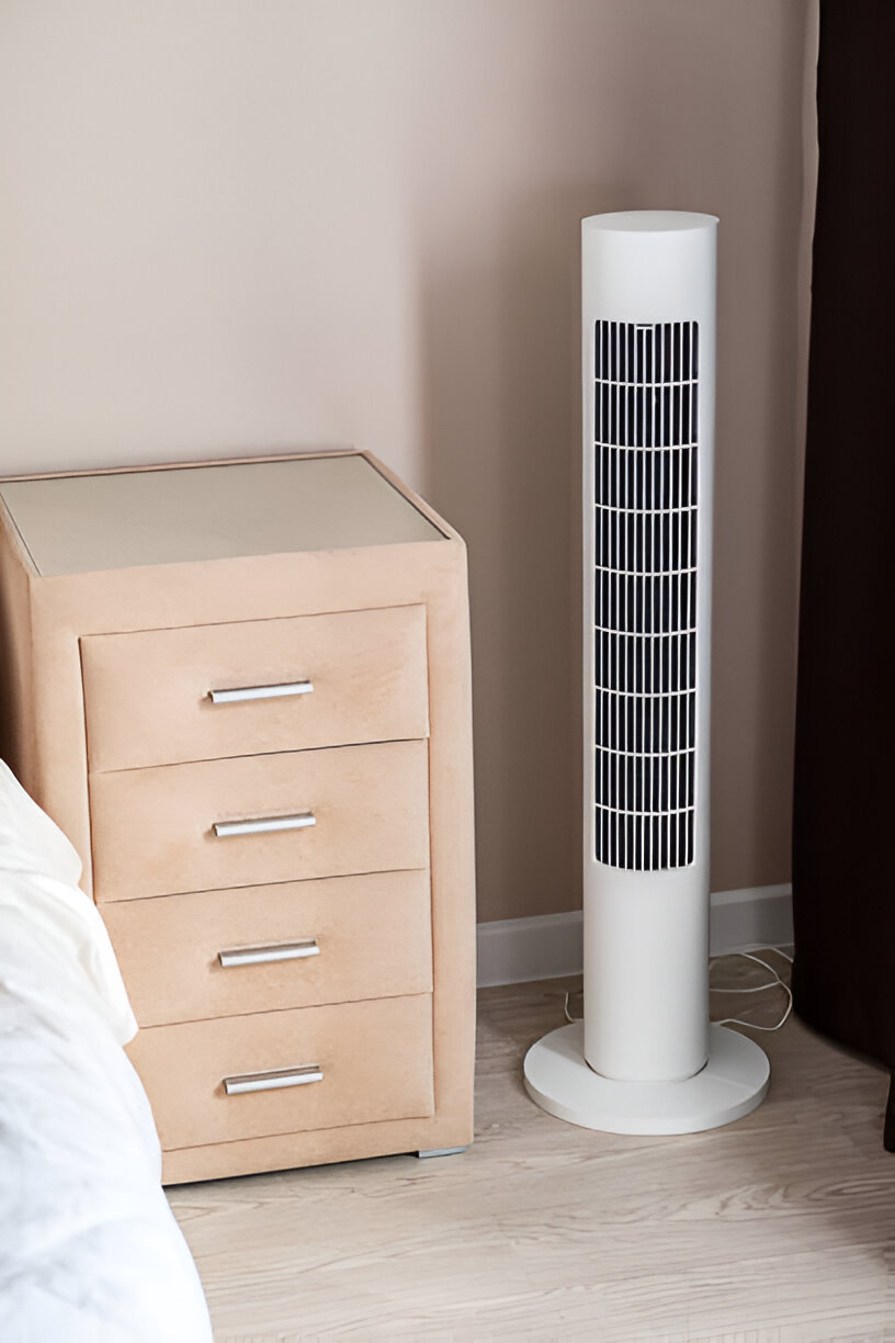 White tower fan next to wooden bedside drawer in minimalist bedroom