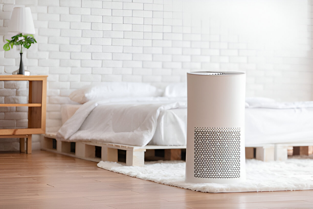Air purifier on white rug near bed with white brick wall background