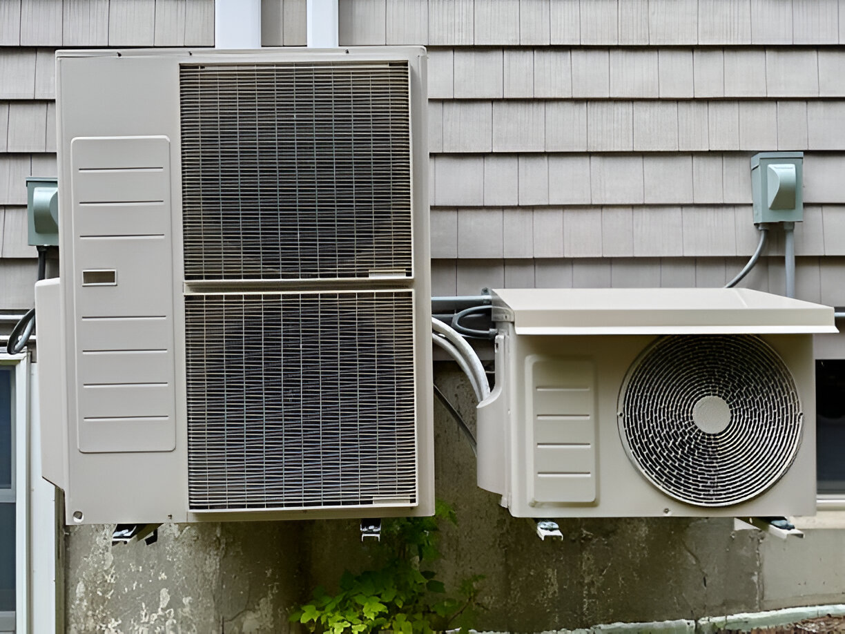 Two white air conditioning units mounted on shingle-sided building exterior
