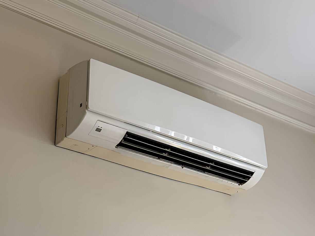 White wall-mounted air conditioning unit with vents near ceiling