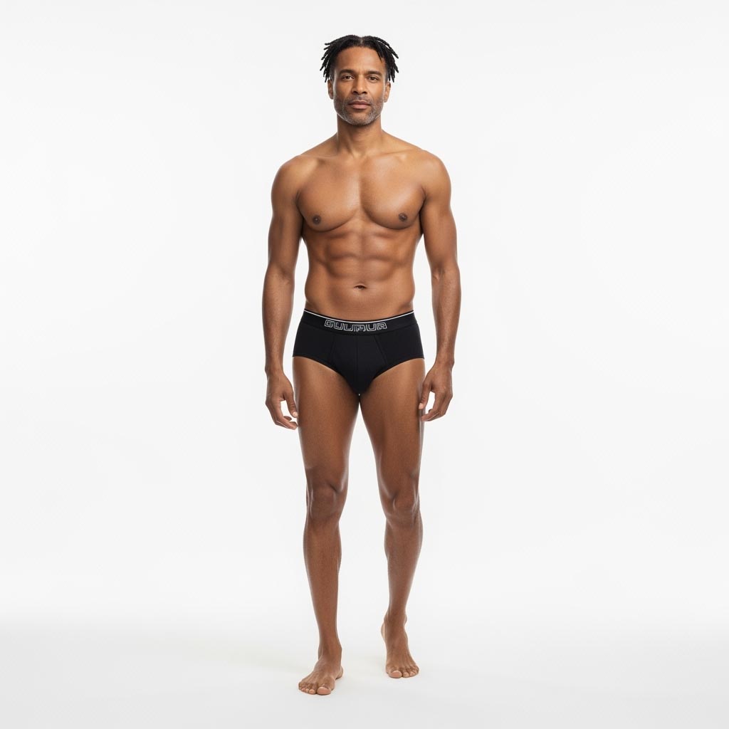 A man with dark, textured hair and a light beard, standing barefoot and wearing black briefs with a white waistband against a white background. He has a muscular physique and looks directly at the camera.