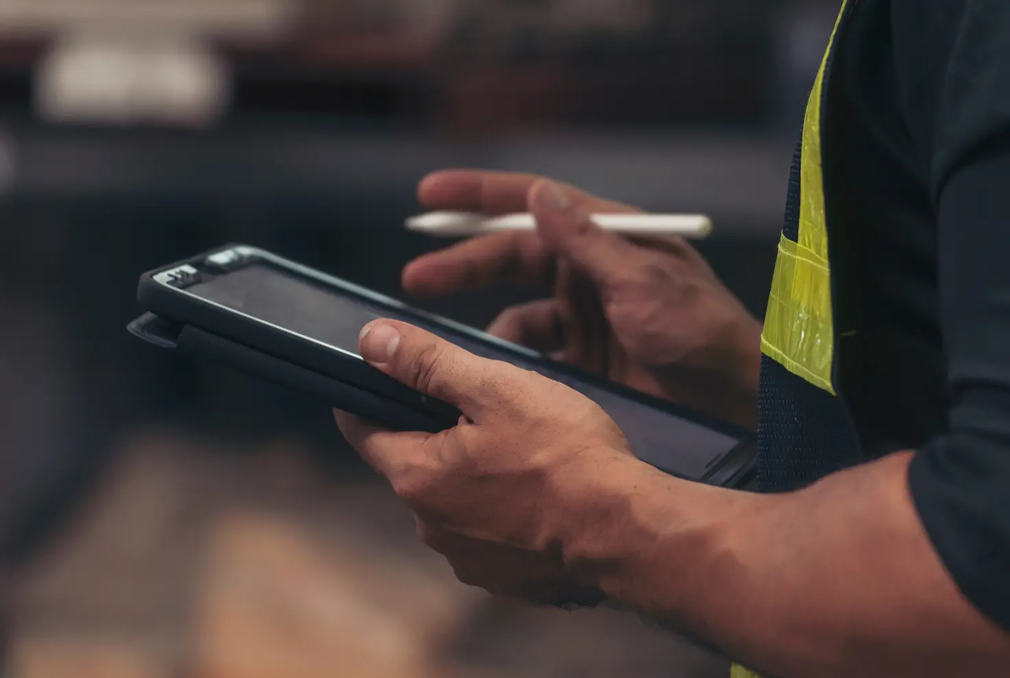Une personne tenant une tablette avec un stylet, portant un gilet de sécurité jaune.