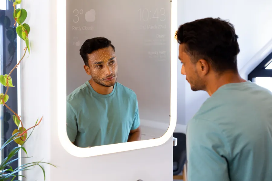 Man with facial recognition dots looking at himself in a smart illuminated mirror.