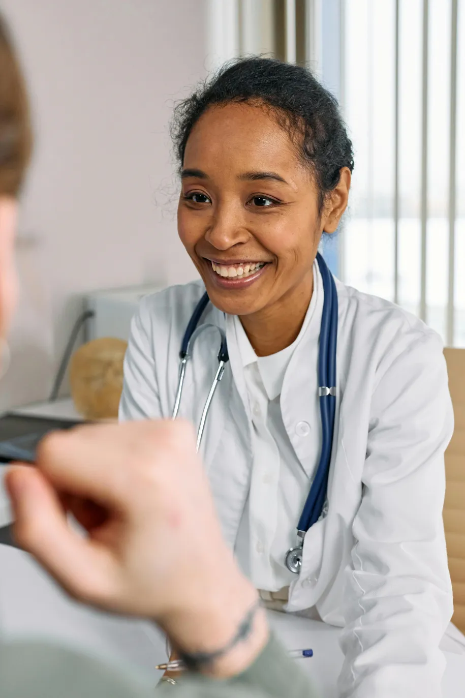 Smiling female doctor with stethoscope speaking to a patient in a medical office.