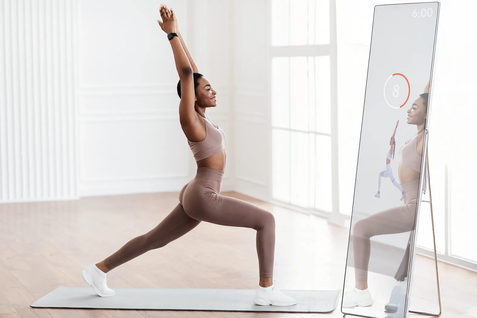 Woman in workout attire doing a lunge stretch in front of a smart mirror displaying a yoga pose and timer.