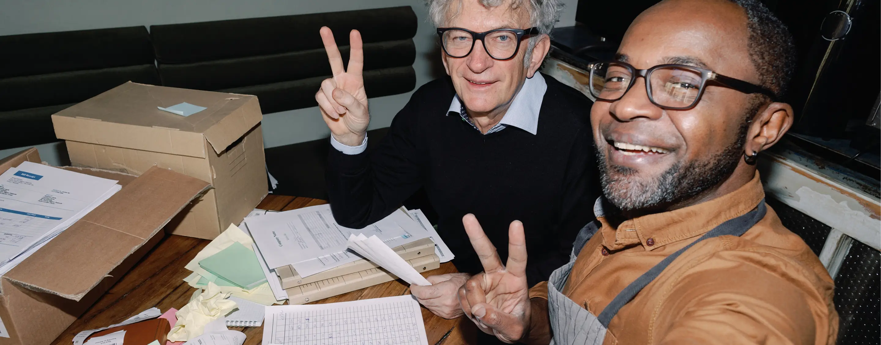 two men give peace sign around paperwork