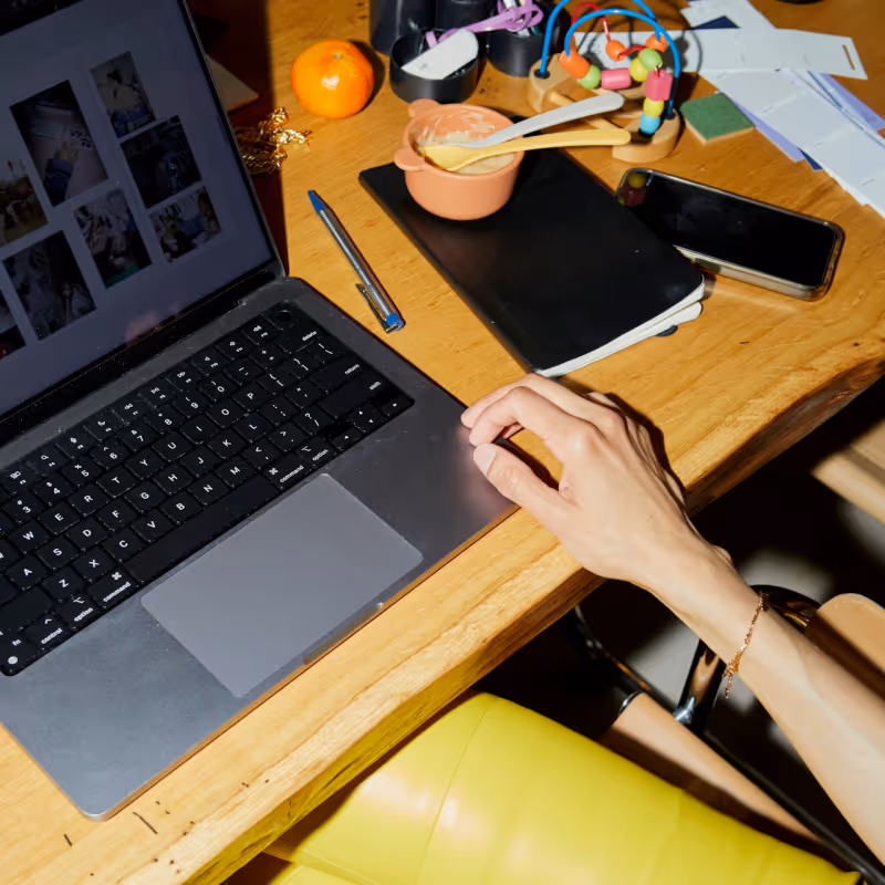 Close-up of a laptop and baby food bowl on a busy wooden desk. 