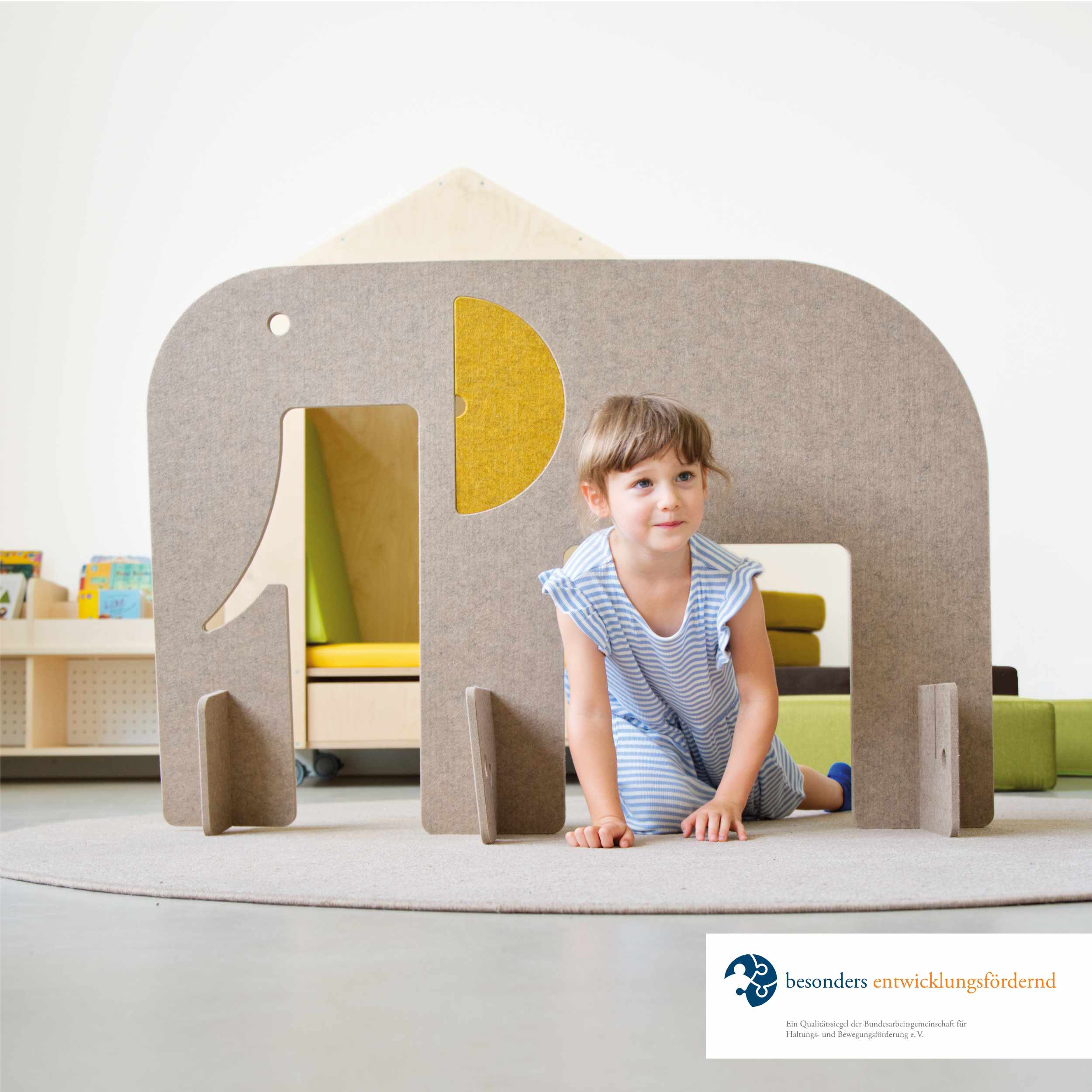 Kleines Mädchen krabbelt unter einem Elefanten aus Filz durch