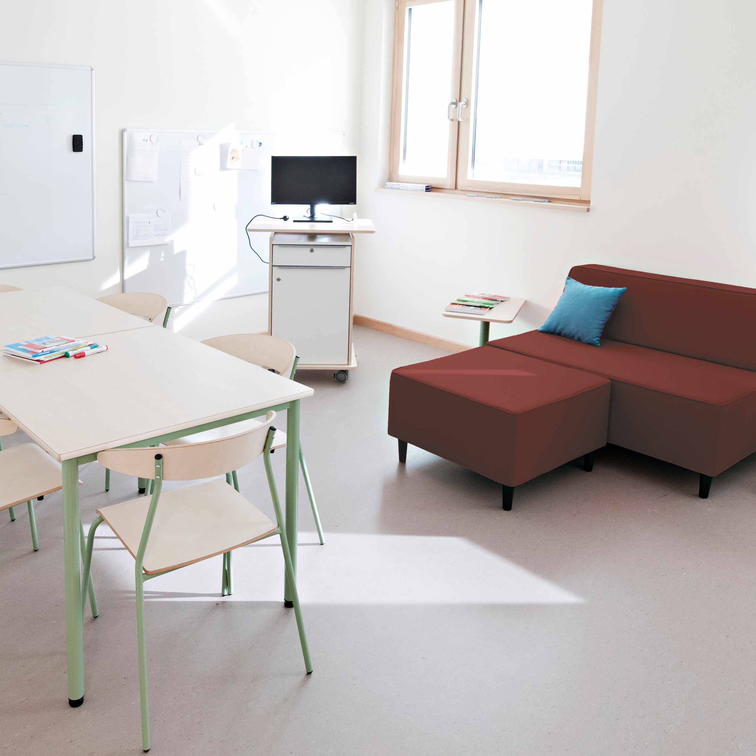 Foto eines Büroraumes mit pinkfarbenem Sofa und Hocker, Stehpult und Arbeitstisch mit Stühlen davor