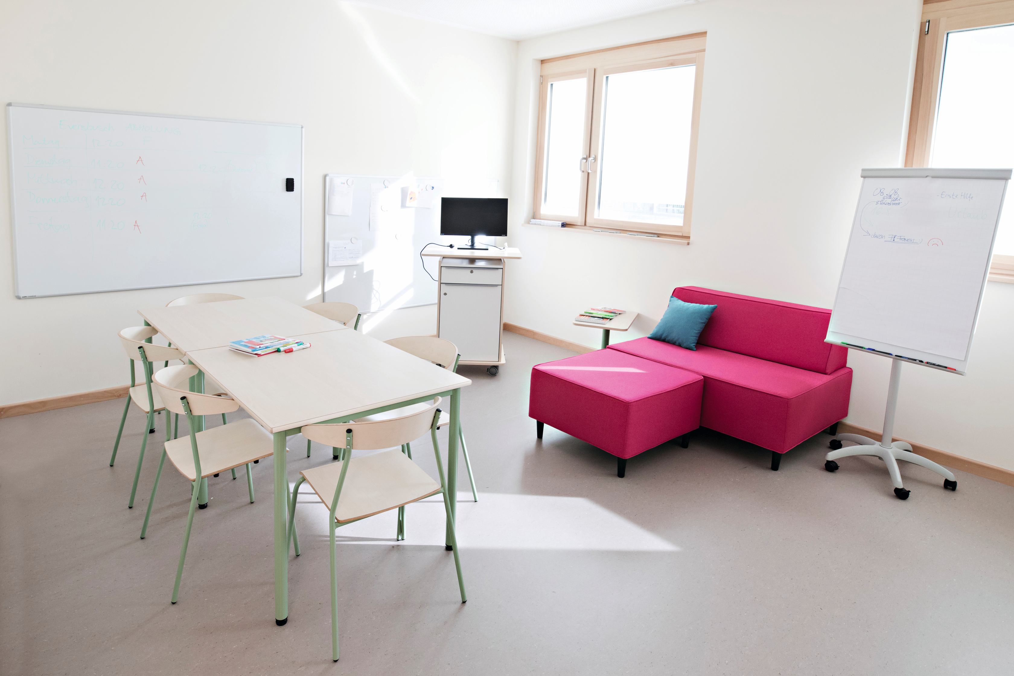 Ein Teamraum in einer Kita mit Besprechungs- und Arbeitstisch, stapelbaren Konferenzstühlen. einem Sofa, einem Stehpult und Flipschart