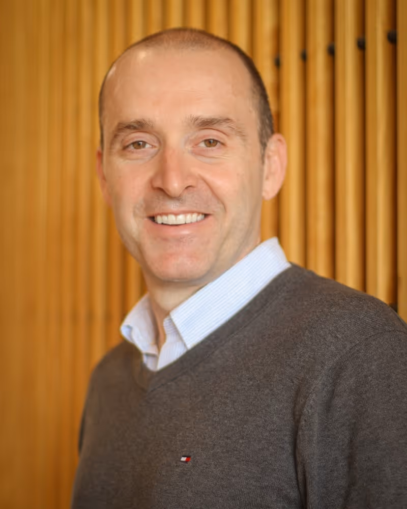 Smiling professional in gray sweater against wooden paneled background
