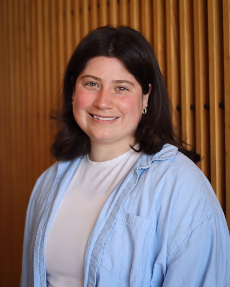 Smiling woman in light blue shirt against wooden paneled background