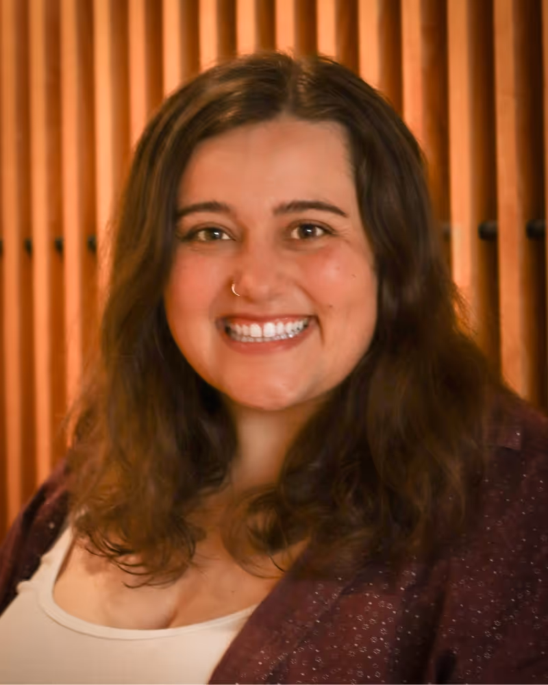 Smiling woman with brown hair in burgundy jacket against orange backdrop