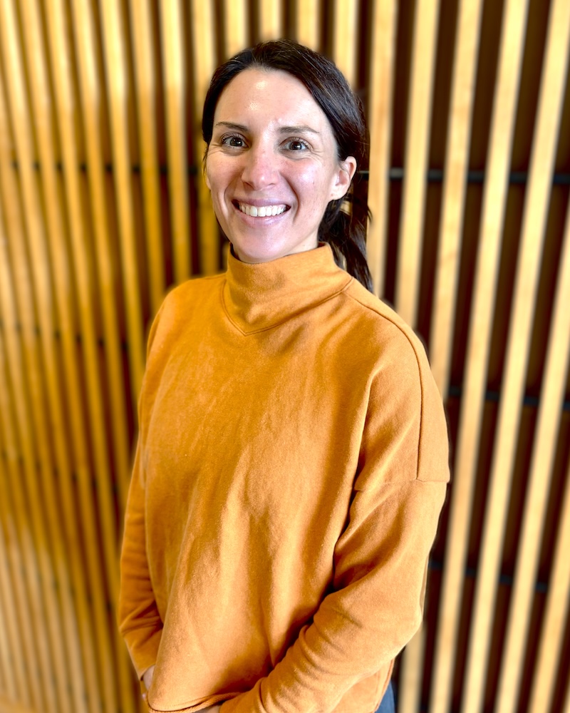 Smiling person in yellow sweater standing in front of wooden slat wall