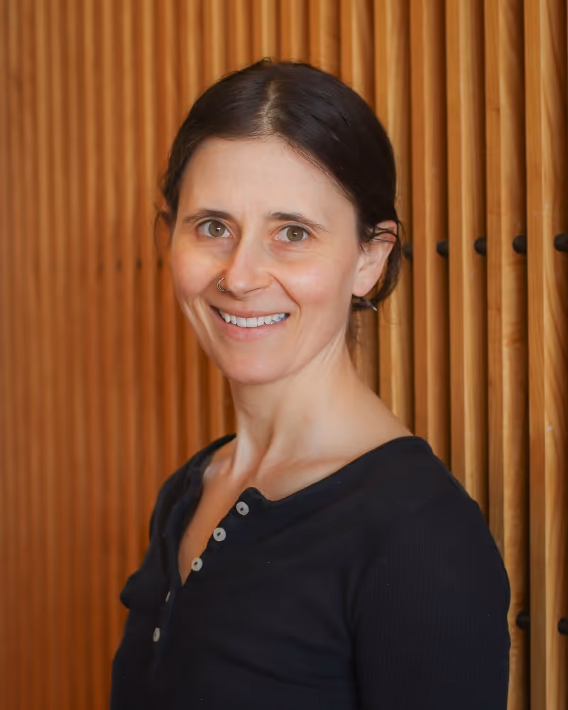 Woman smiling at camera wearing black button-up top against wooden wall