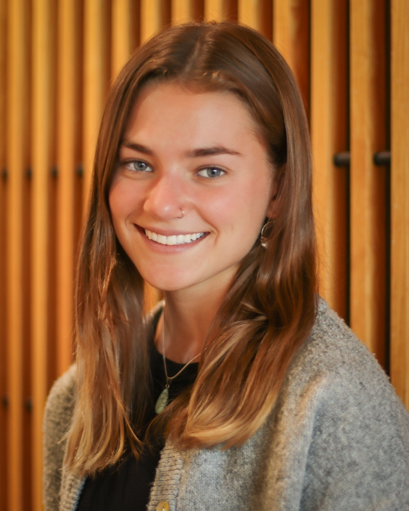 Woman with brown hair smiling at camera in front of gold curtains