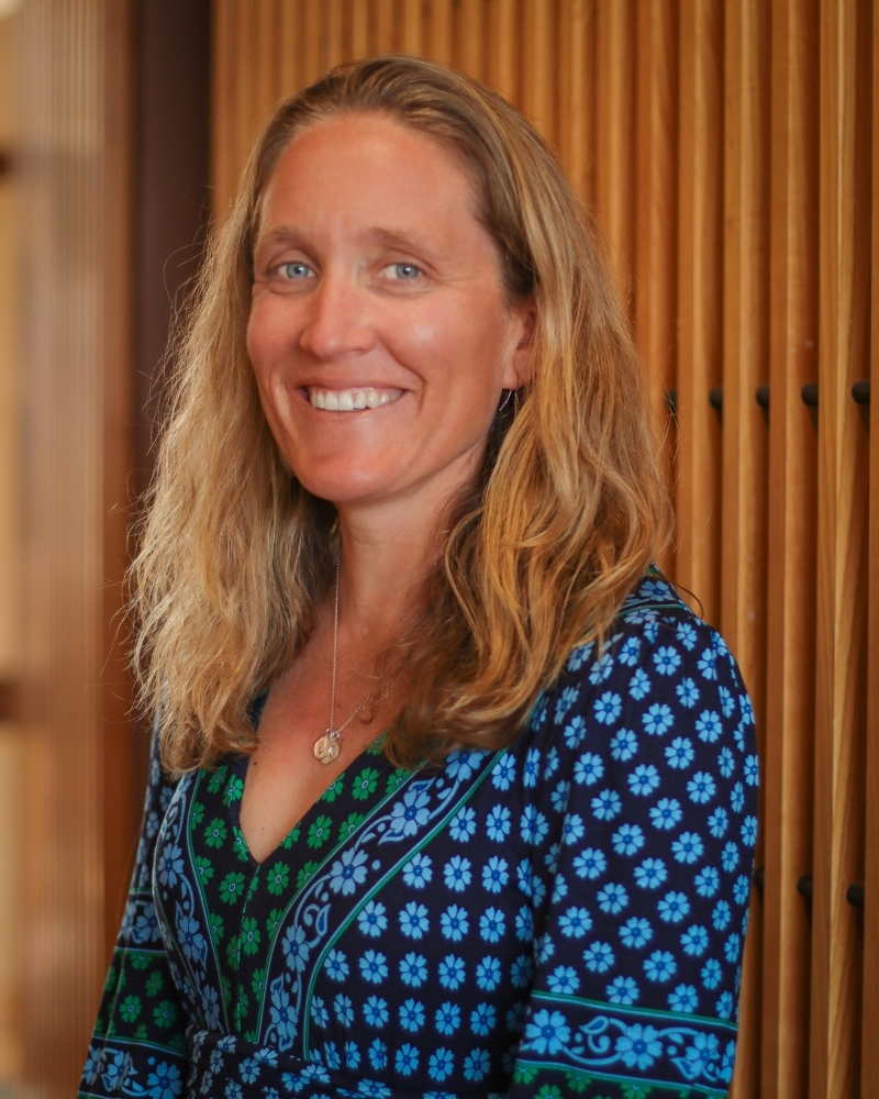 Woman with long brown hair smiling, wearing patterned blue and green dress