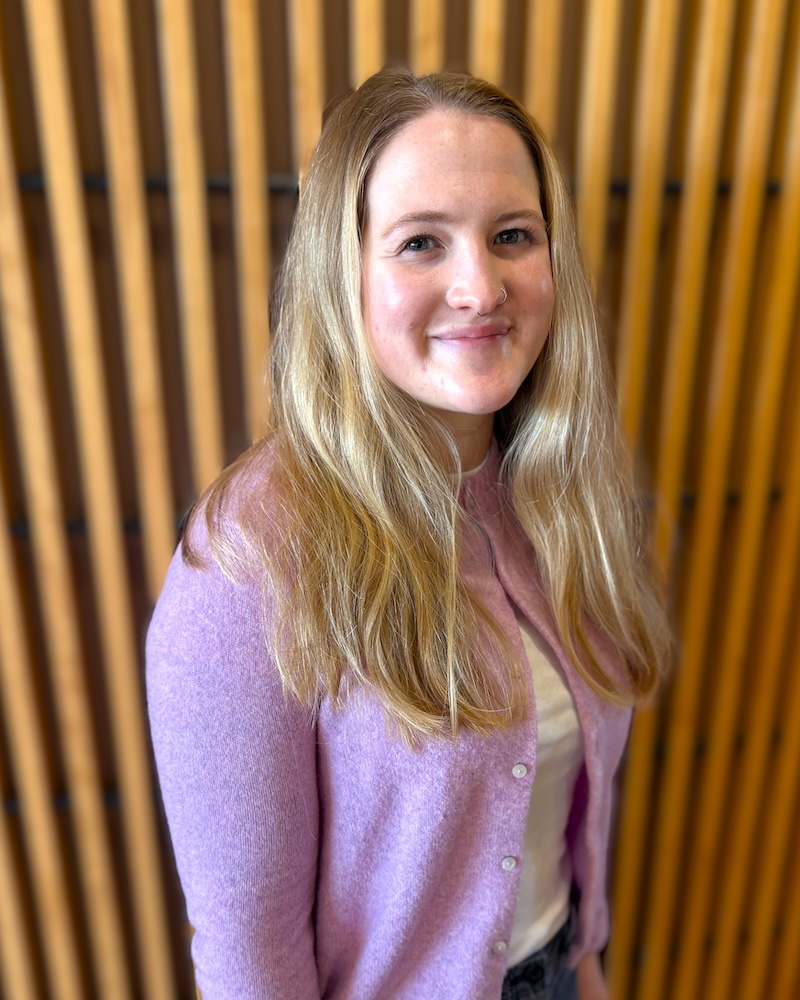 Portrait of a young woman with long brown hair wearing a lavender cardigan indoors