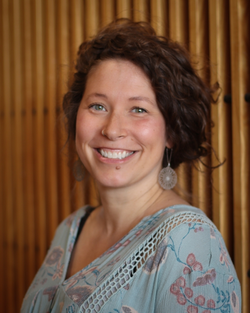 Woman smiling warmly at camera wearing patterned blue blouse with dangling earrings