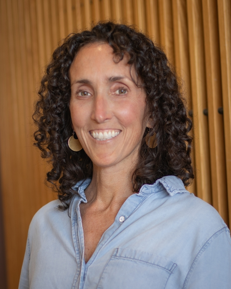 Woman with curly dark hair smiling at camera wearing light blue shirt