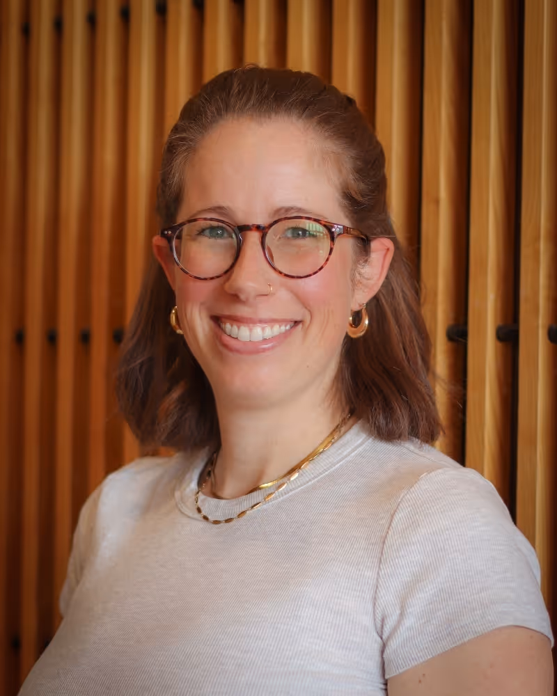 Woman with glasses smiling at camera against golden curtain backdrop