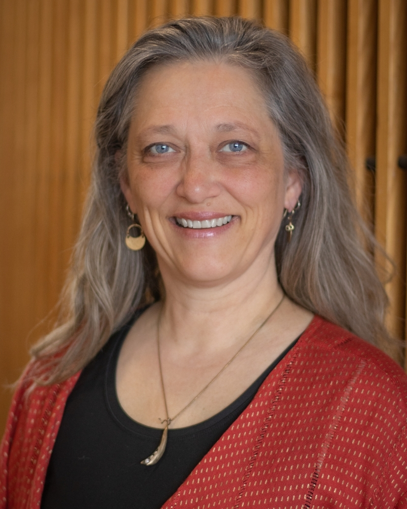 Smiling woman with long gray hair wearing red cardigan and black top