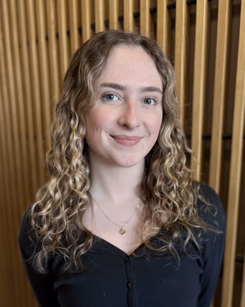 Portrait of a woman with long wavy blonde hair wearing a black top against striped background