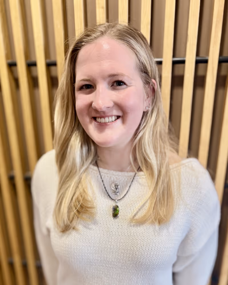 Smiling woman with long blonde hair wearing white sweater and pendant necklace