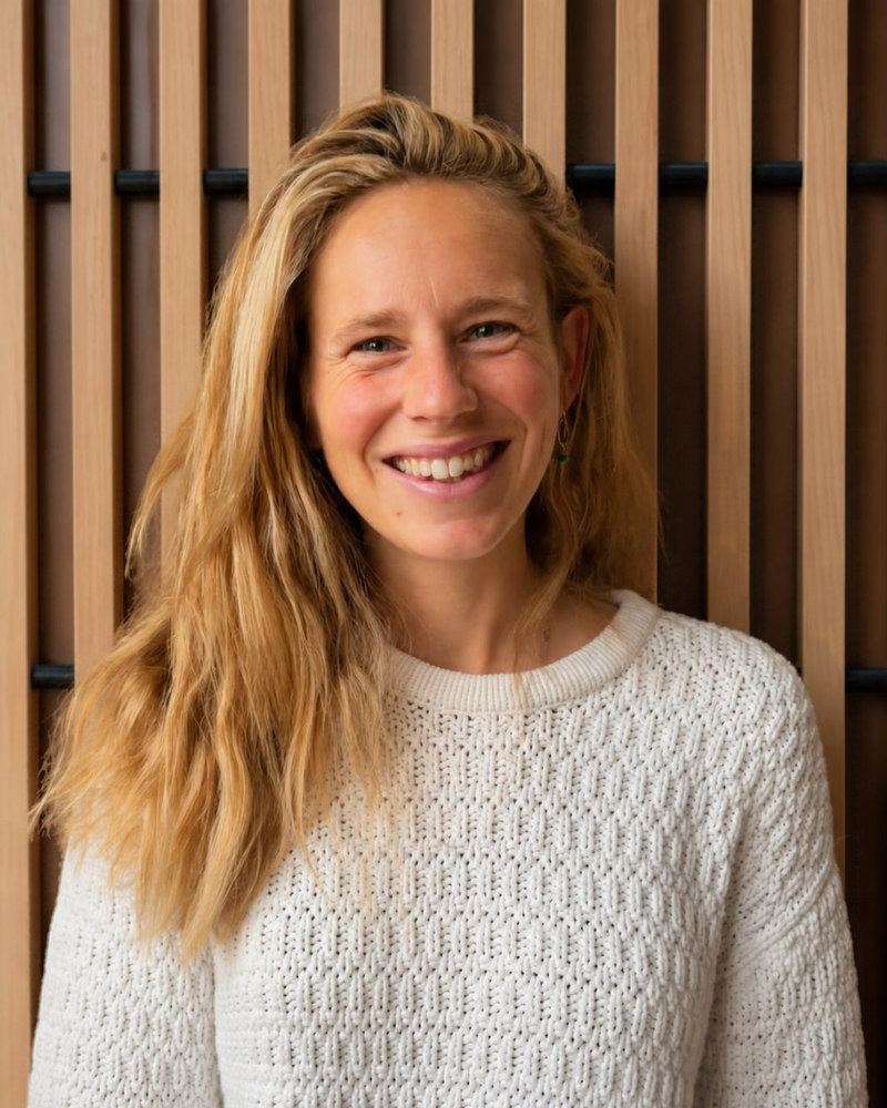 Smiling woman with long strawberry blonde hair wearing cream-colored sweater against wooden slats