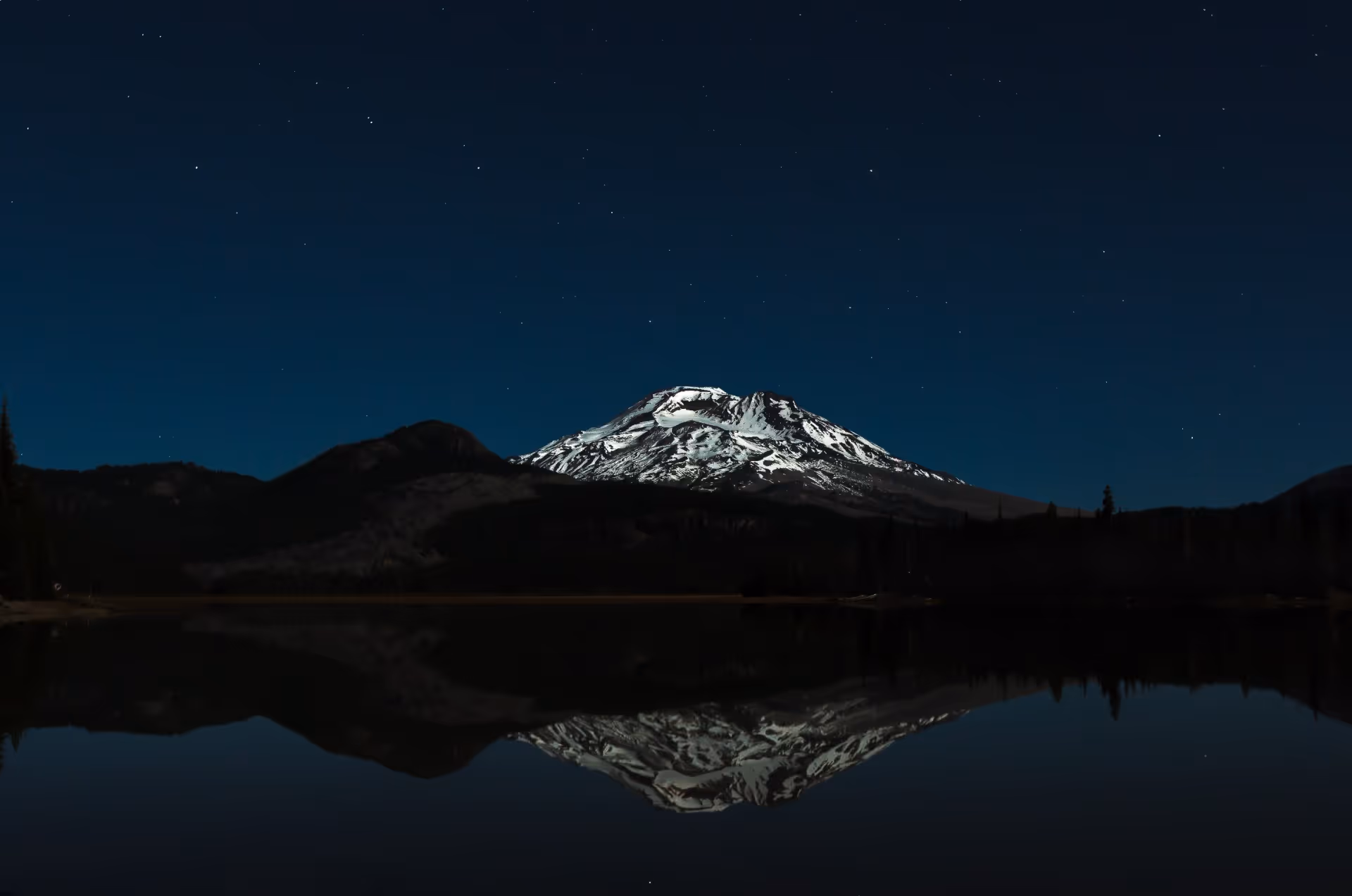 Dark lake reflecting a mountain under a night sky.