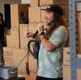 A man standing in a warehouse holding a hair dryer.