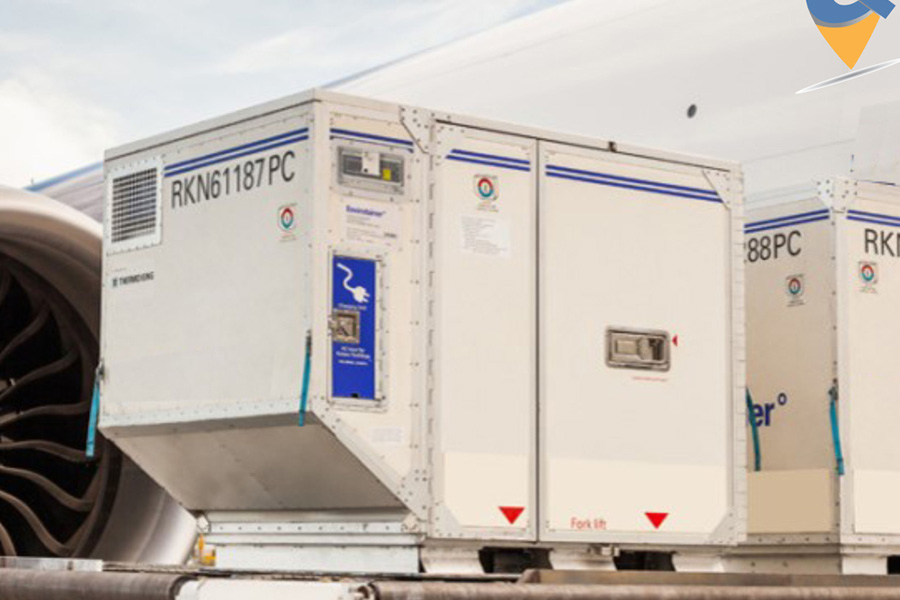 A large cargo aircraft operated by Pacific Air Cargo is seen on an airport tarmac with its nose lifted open to allow for front-loading of oversized freight. A massive wooden crate is being loaded into the aircraft using a heavy-duty scissor lift platform. Several ground crew members in high-visibility jackets are assisting with the operation, while others stand near a set of mobile stairs leading into the aircraft. The plane is a Boeing 747-400F, identifiable by its four engines and distinctive hump-shaped upper deck. The bright blue sky and modern terminal buildings in the background suggest a busy international airport setting. The scene captures the scale and precision of Pacific Air Cargo's logistics operations, highlighting their capability to handle oversized and high-value cargo.