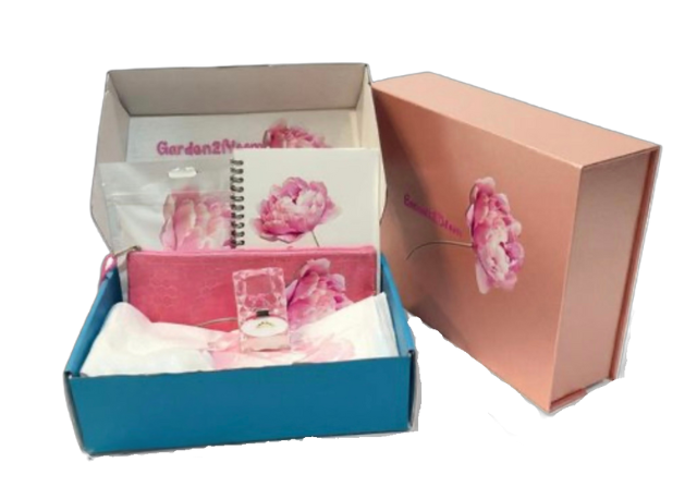Open gift box containing pink floral-themed stationery including a notebook, pouch, and a small clear box, next to a closed pink cover box with a flower design.