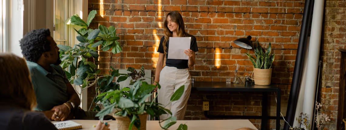 A founder presenting a vision to a small team in a warm, plant-filled office — symbolising the shift from personal pitching to scalable marketing support.