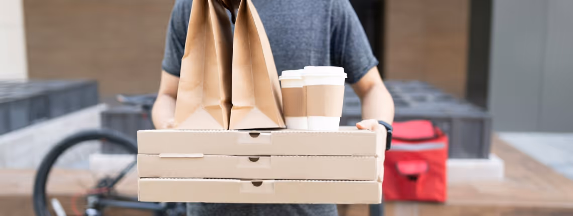 Person carrying a tray of takeaway coffee cups and food boxes — symbolising the typical ‘order-taker’ role many agencies settle for instead of being true strategic partners.