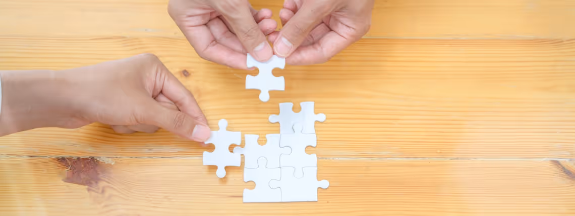 Hands fitting puzzle pieces together on a wooden table — symbolising unified marketing efforts connecting seamlessly