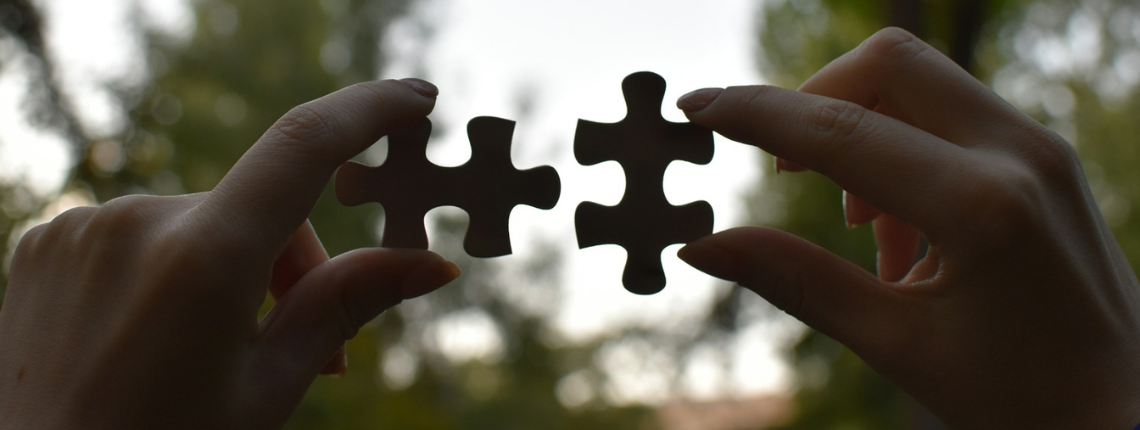 Two hands holding mismatched puzzle pieces against a soft sunset background — symbolising the alignment gap between founders and marketers.