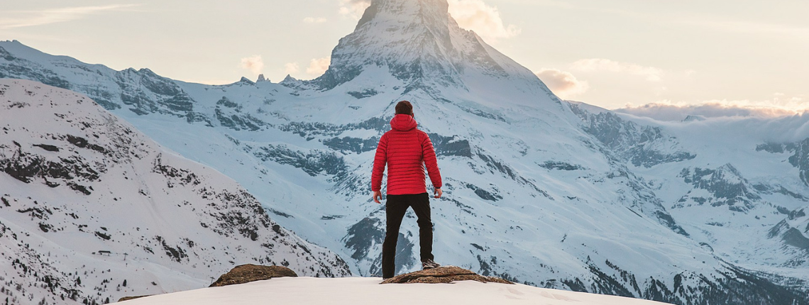 Solo founder in a red jacket standing at the base of a vast snowy mountain — symbolising courage to move forward despite fear.