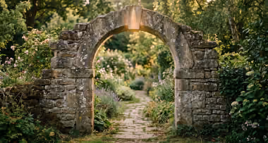 An old stone archway in a garden, its keystone lit by the afternoon sun.