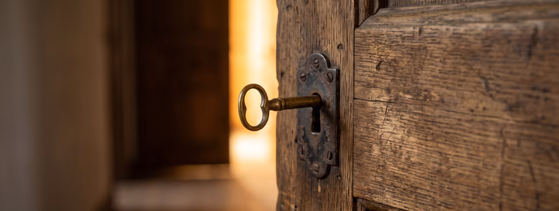 An old wooden door slightly open, with a brass key in its lock and warm light spilling through.