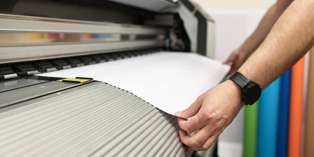 Hands loading paper into a large format inkjet printer