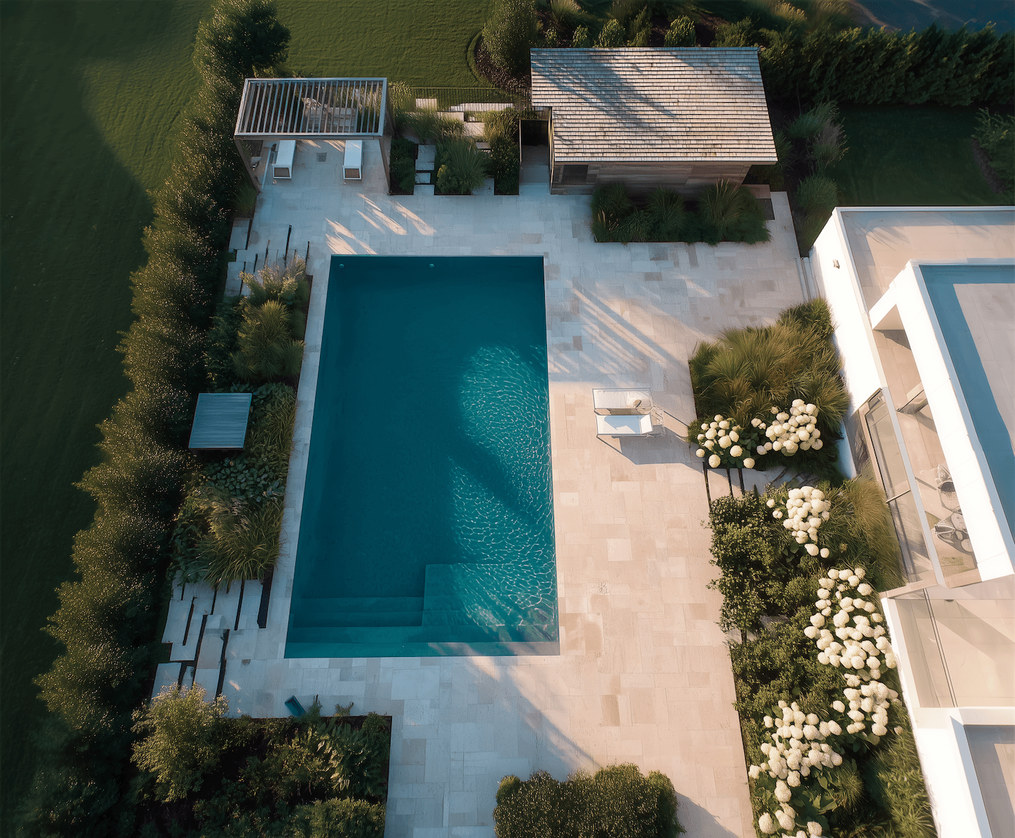 Modern rectangular swimming pool with a stone patio, pergola, and cabana, showcasing a high-end landscape construction project.