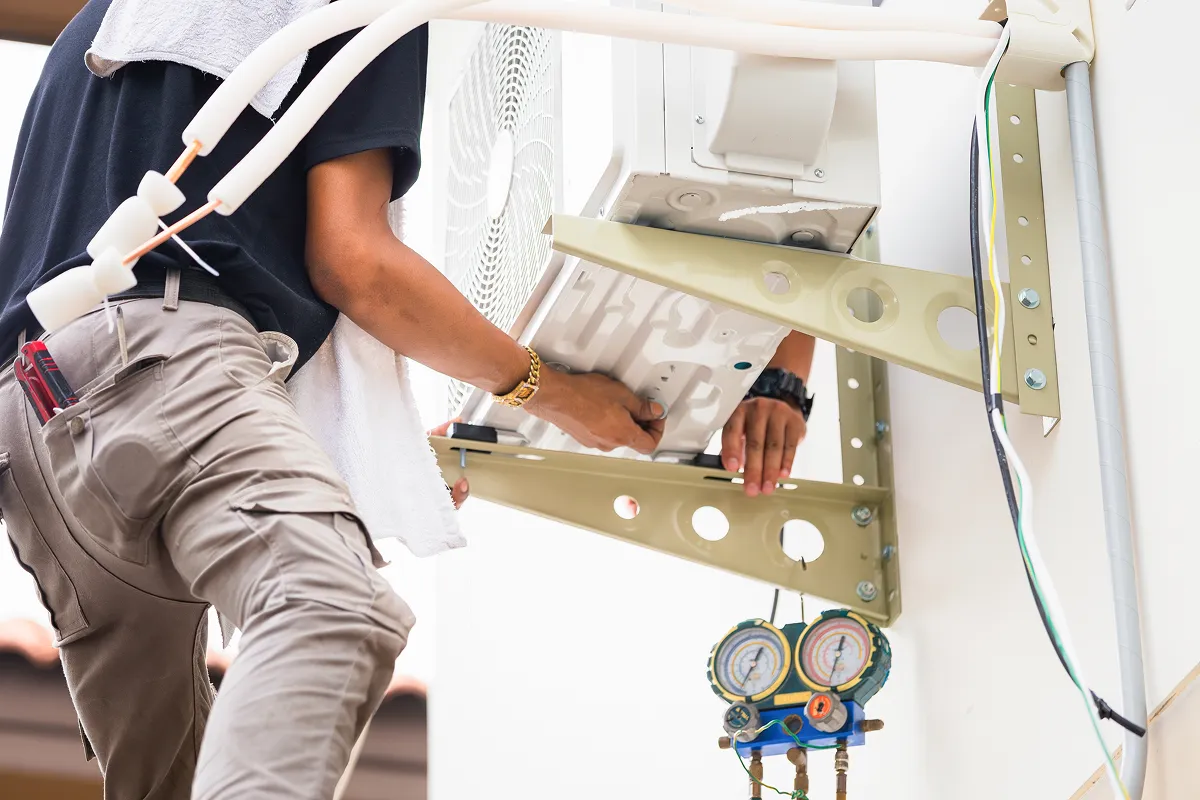 A technician installs an air conditioning unit while checking pressure gauges.
